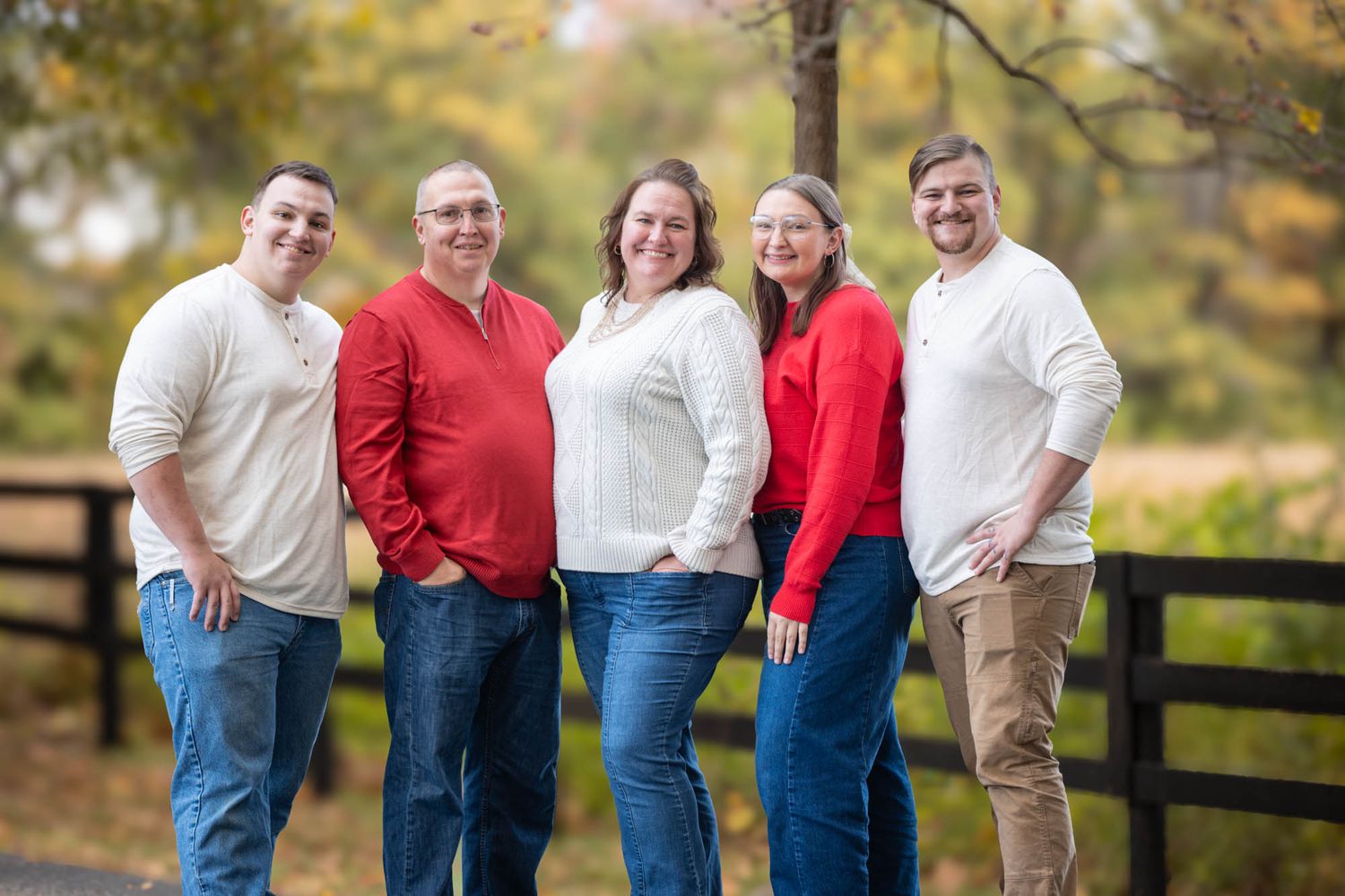 Family of five smiling together outdoors in red and white outfits during autumn foliage season.