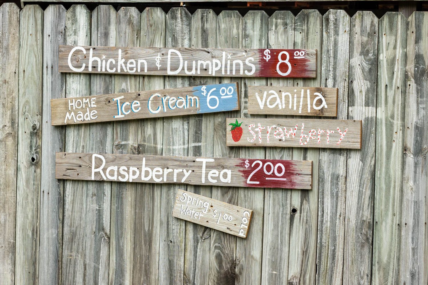 Rustic wooden signs on a fence advertising chicken dumplings, homemade ice cream, and raspberry tea.