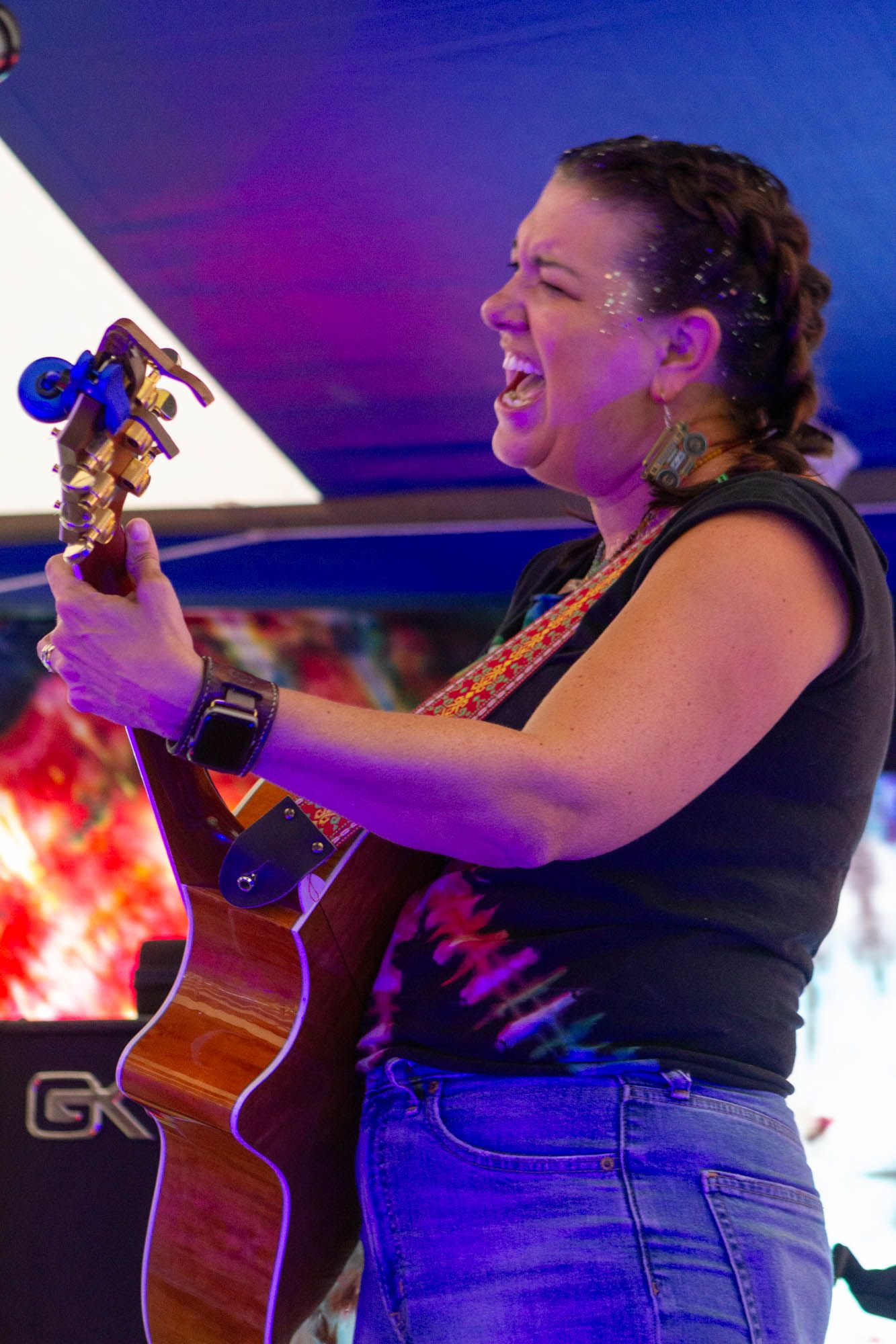 Female vocalist passionately sings while playing acoustic guitar on stage with tie-dye backdrop.