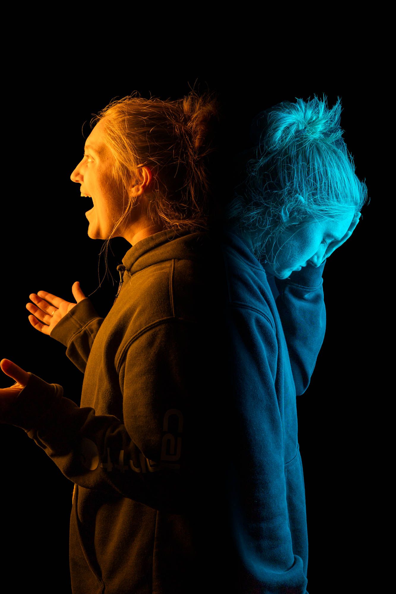 Woman in hoodie photographed back-to-back in warm orange and cool blue light showing expressive emotional contrast.