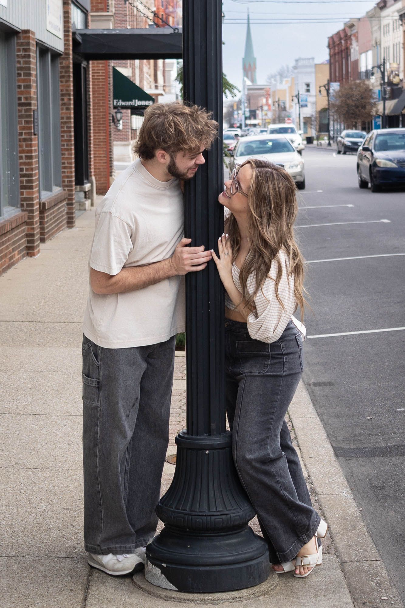 Romantic couple leaning around a black street lamp post on a charming urban sidewalk.