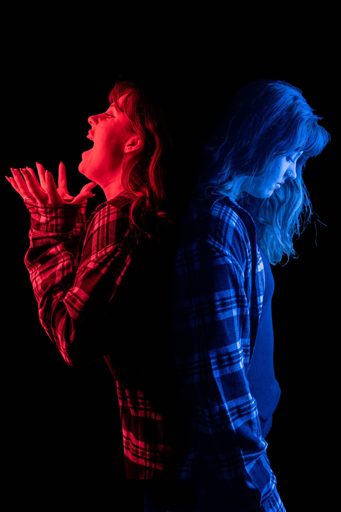 Double exposure portrait of woman in plaid shirt lit in red and blue showing contrasting emotional states.