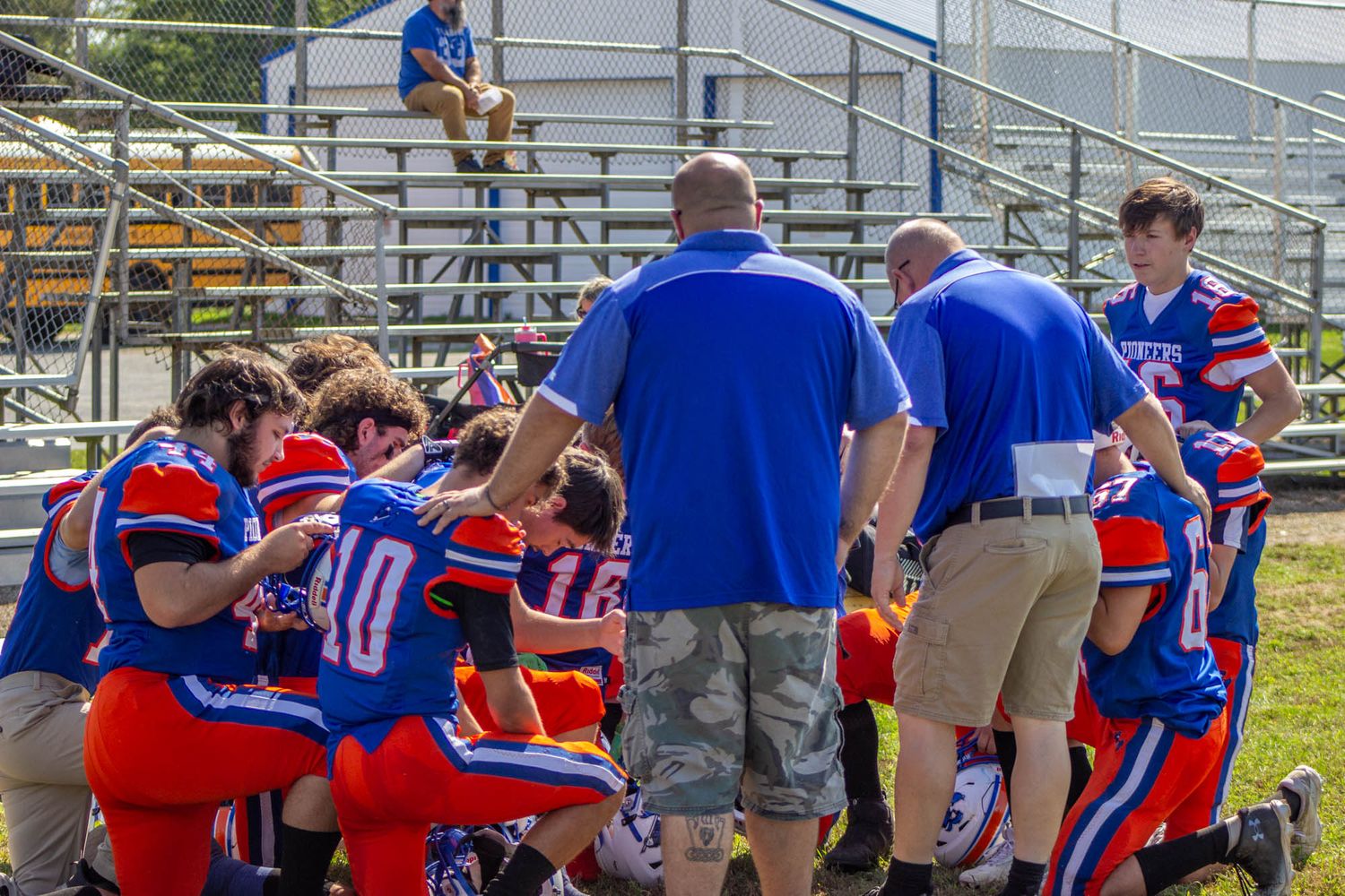 Pioneers football team huddles with coaches on the sideline during a youth football game.