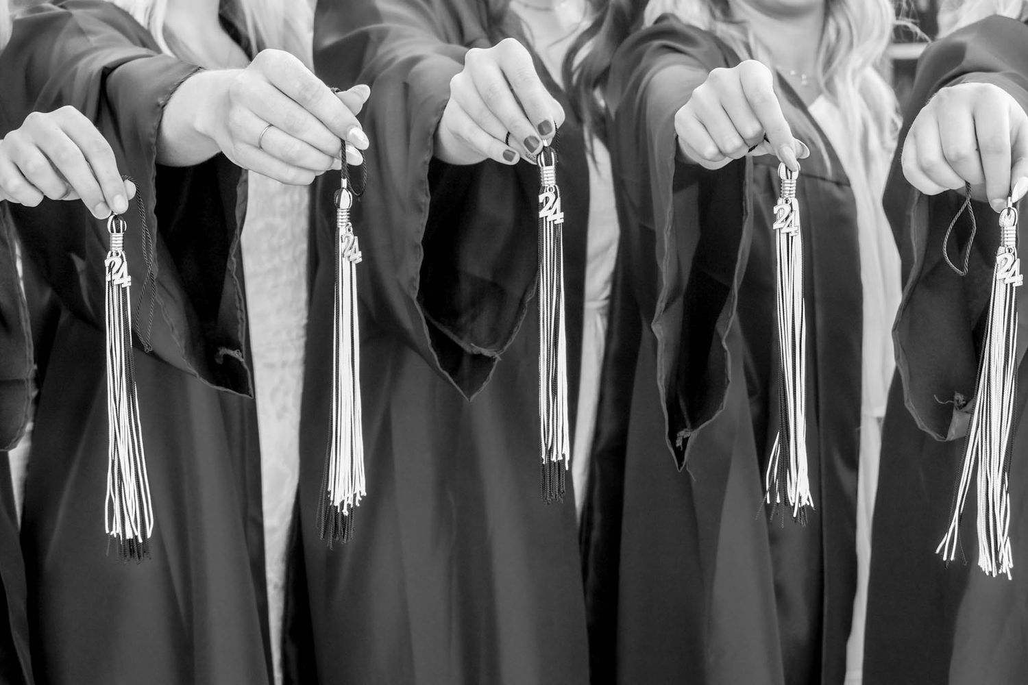 Black and white photo of graduates in gowns holding diploma tassels at graduation ceremony.