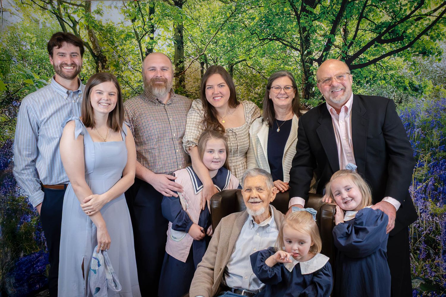 Multi-generational family portrait posing together in front of scenic forest backdrop.