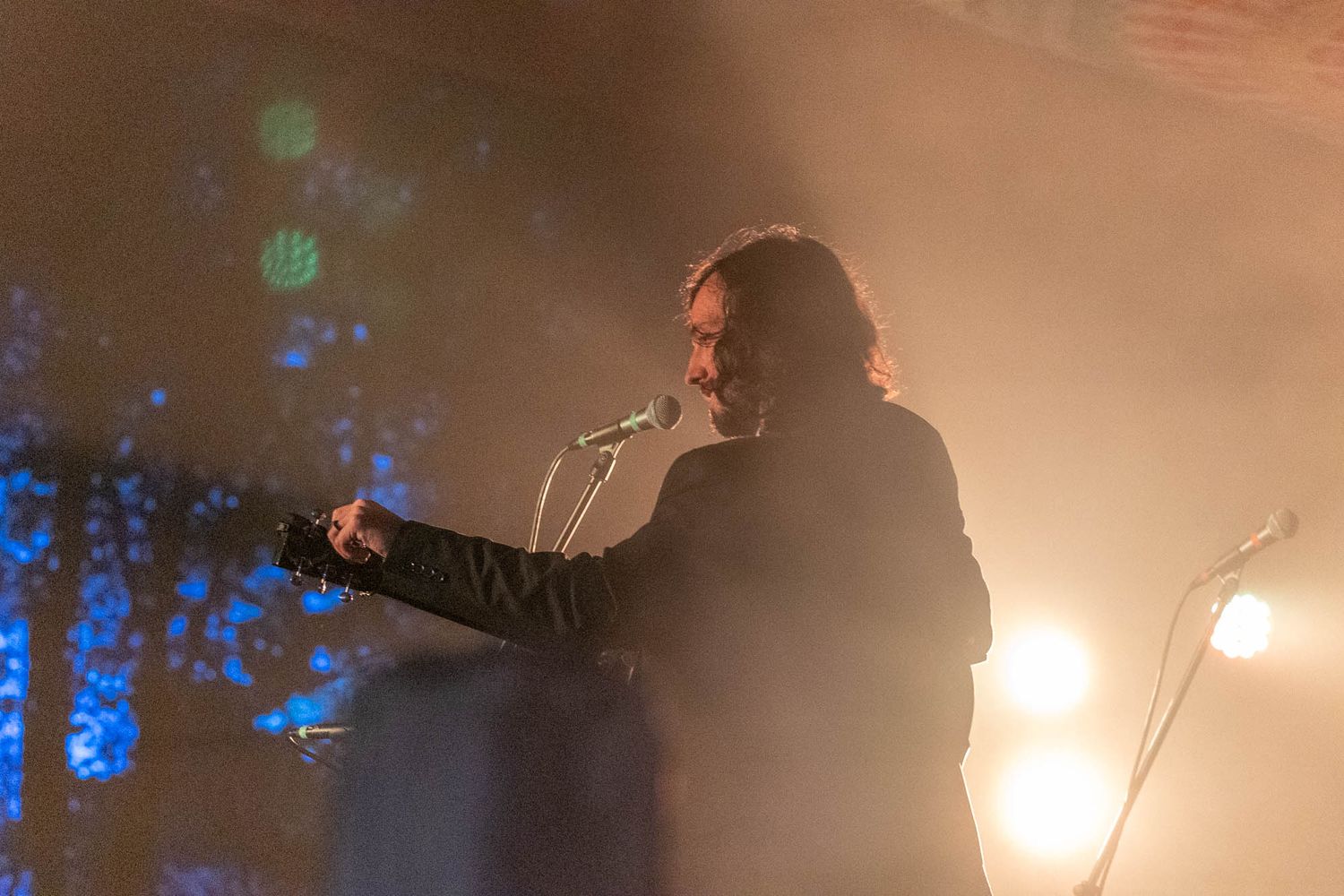 Silhouetted guitarist performs on foggy stage with blue atmospheric lighting behind them.