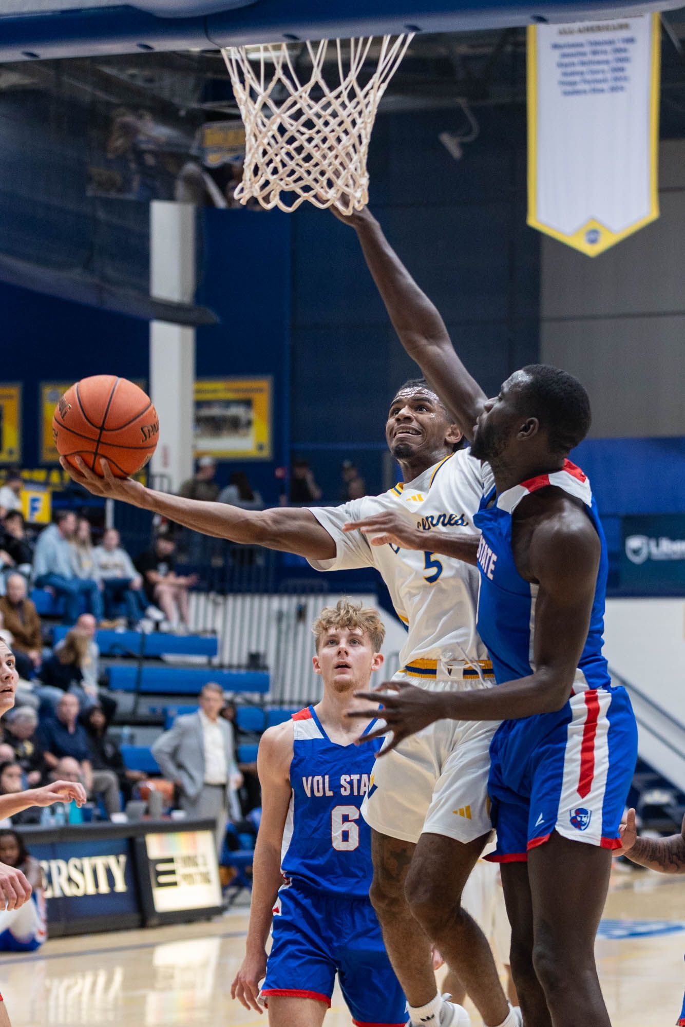 Vincennes University basketball player drives to basket past Vol State defender number 6 during college game.