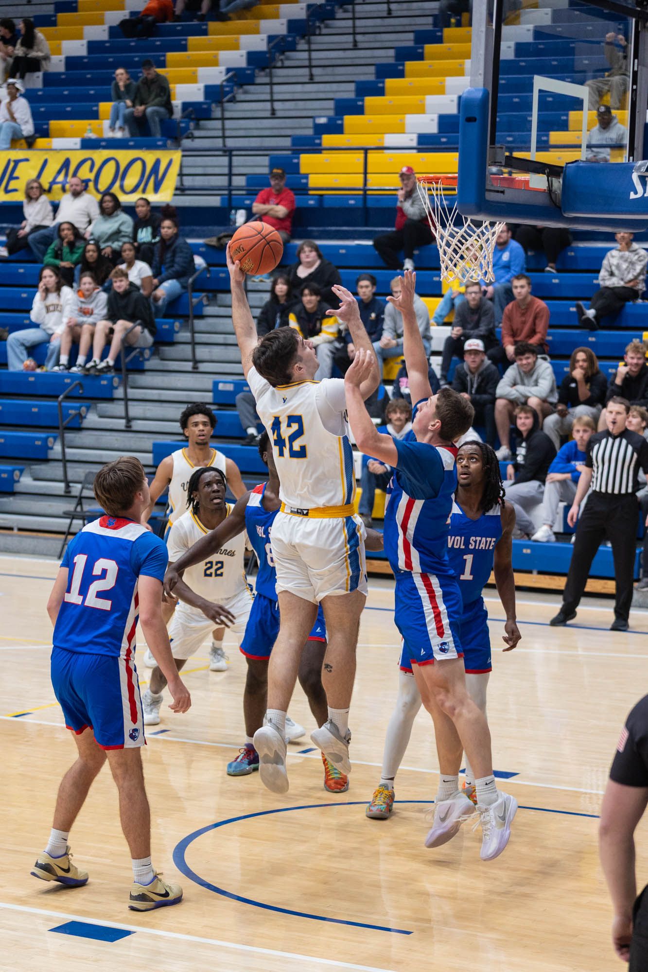 Vincennes University basketball player number 42 attempts layup against Vol State defenders during college game.