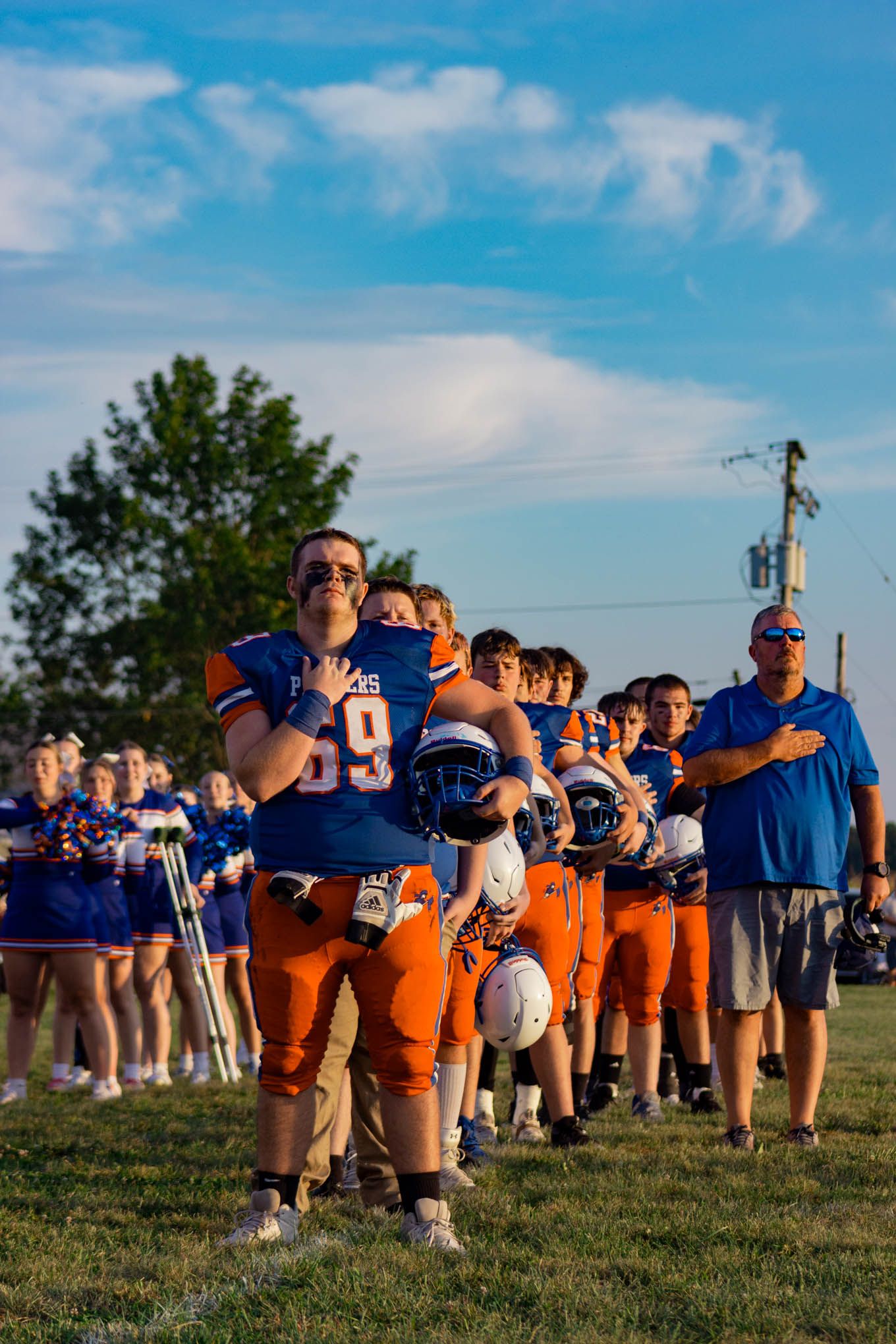 Pioneer football player number 69 stands with hand over heart during national anthem before a game.