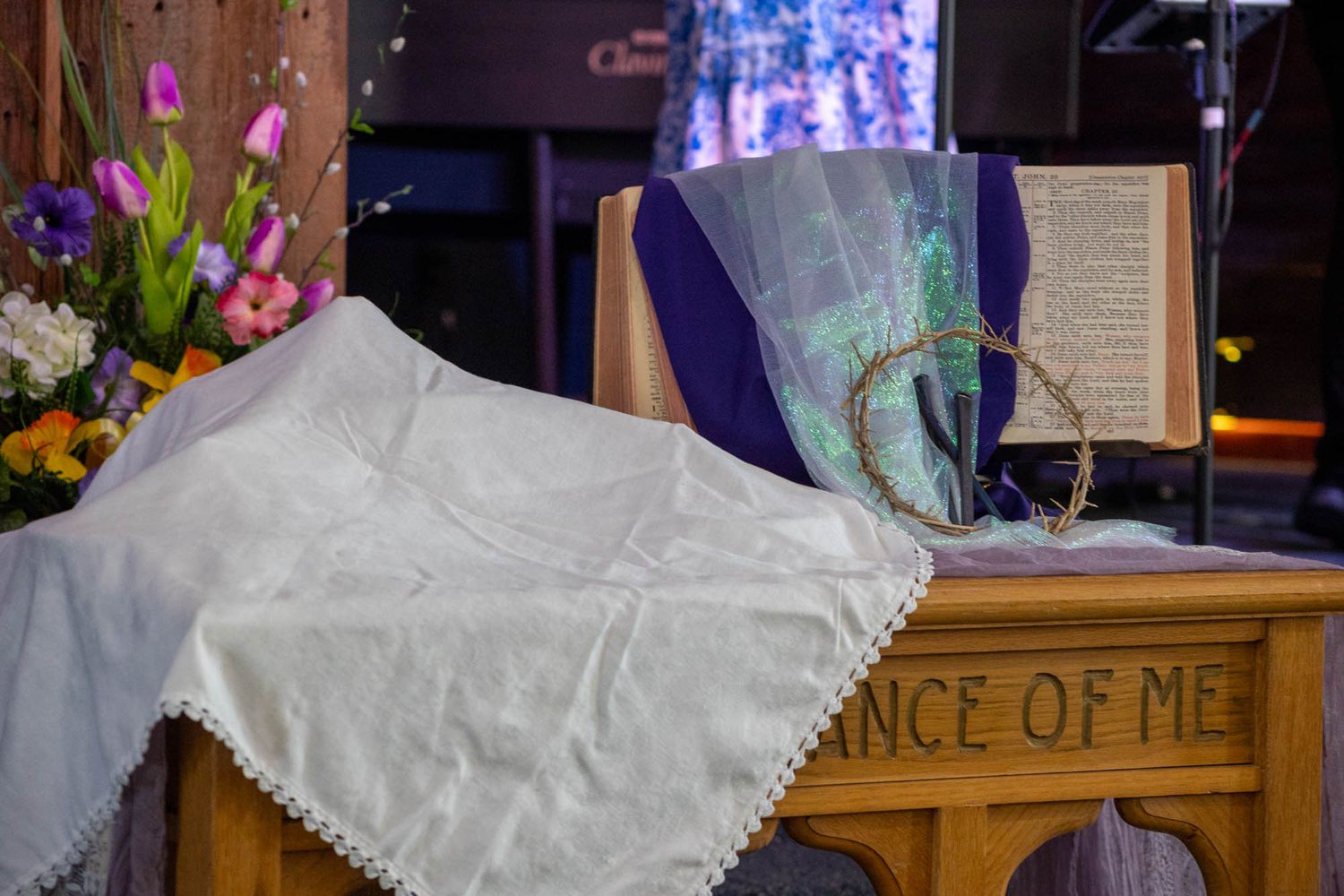 Church altar display with white cloth, crown of thorns, and open Bible on wooden pulpit.