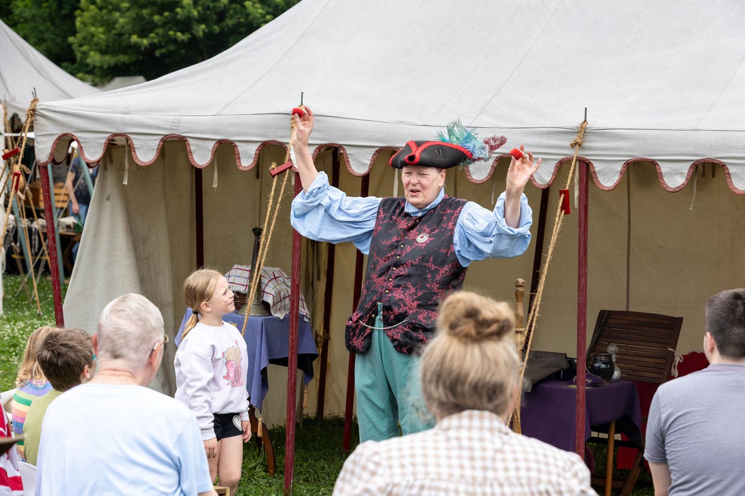 Medieval performer in costume entertains crowd at outdoor Renaissance fair tent event.