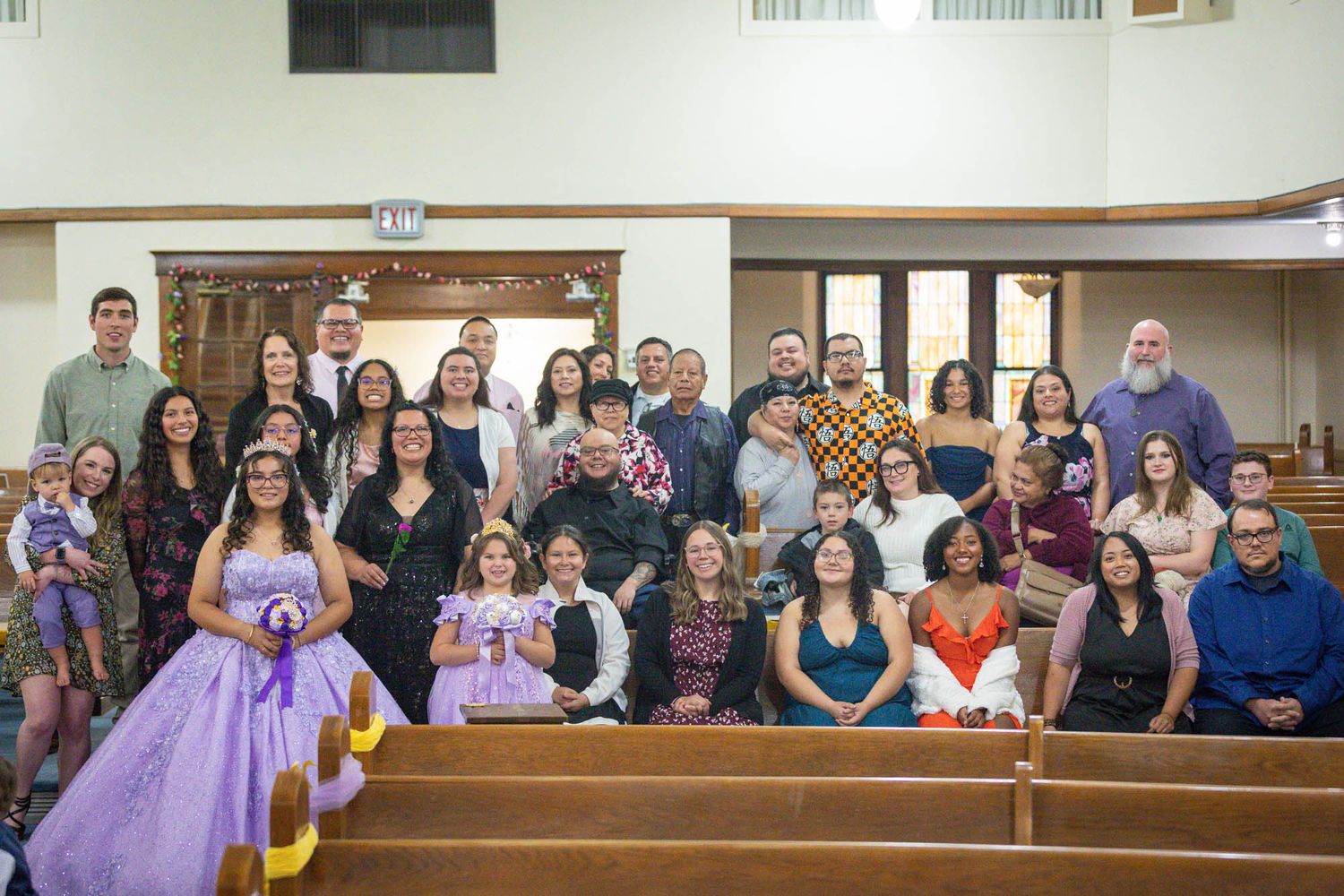 Large group of quinceañera guests pose together in church pews for a group photo.