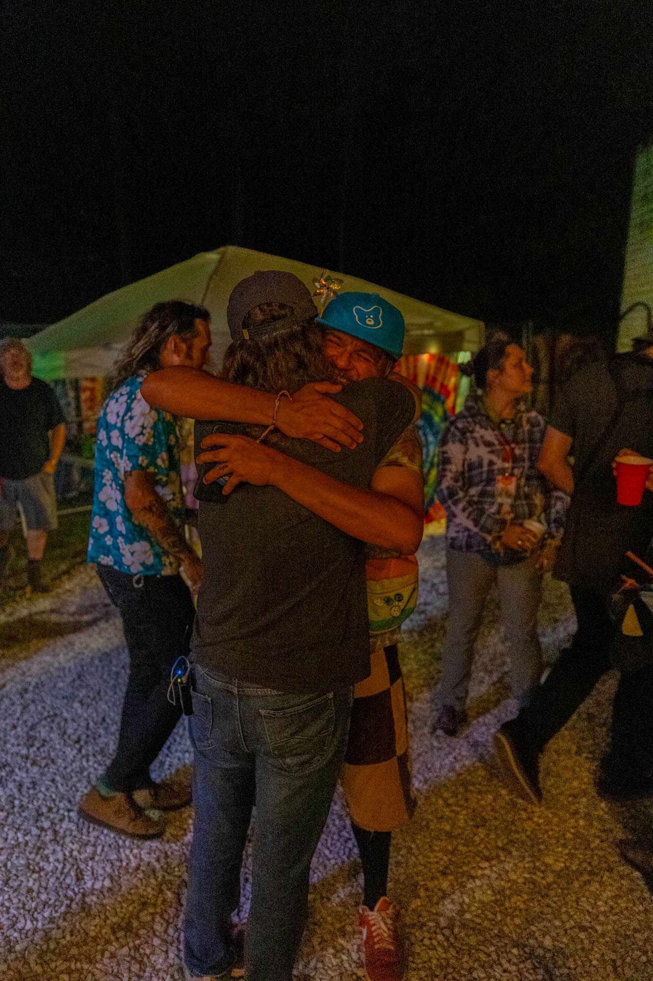 Two people sharing a warm hug at an outdoor music festival at night.