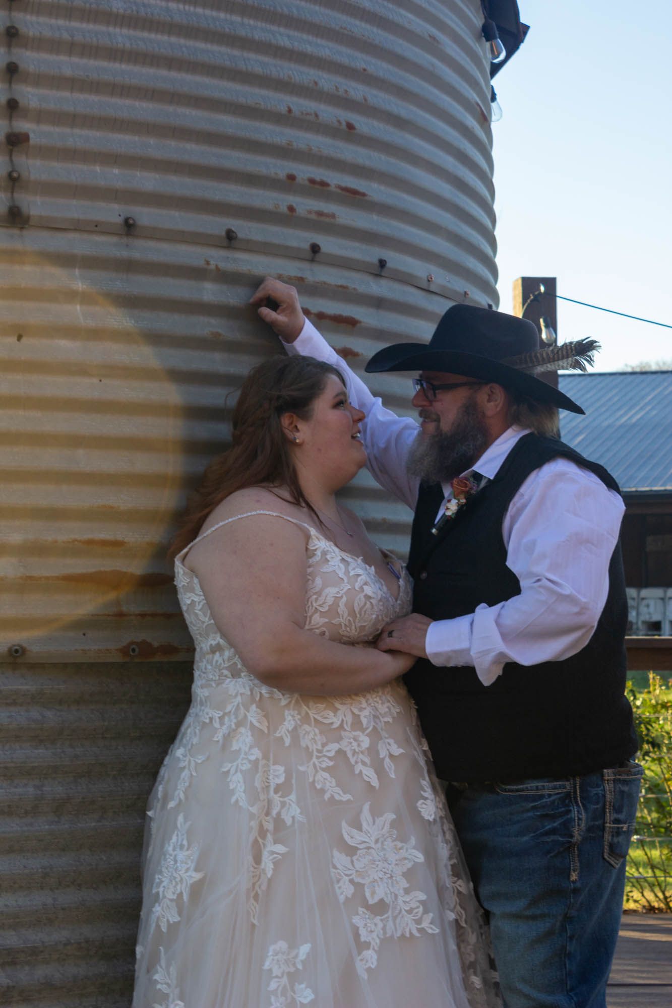 Bride and groom share a romantic moment near a rustic grain silo at their country western wedding.