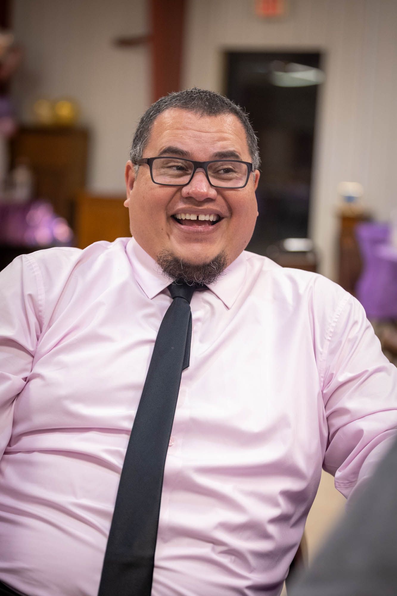 Happy Latino man in pink shirt and black tie smiling at quinceañera.