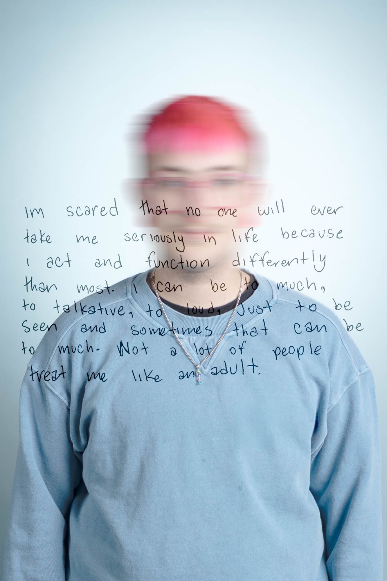 Person with pink hair and blurred face wearing blue sweater with handwritten text overlay expressing fear of not being taken seriously.