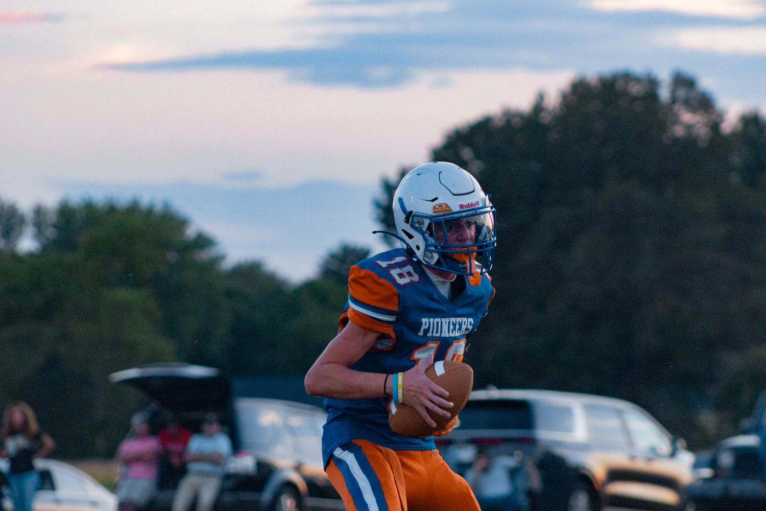 Pioneer football player in blue and orange uniform runs with the ball under a twilight sky.