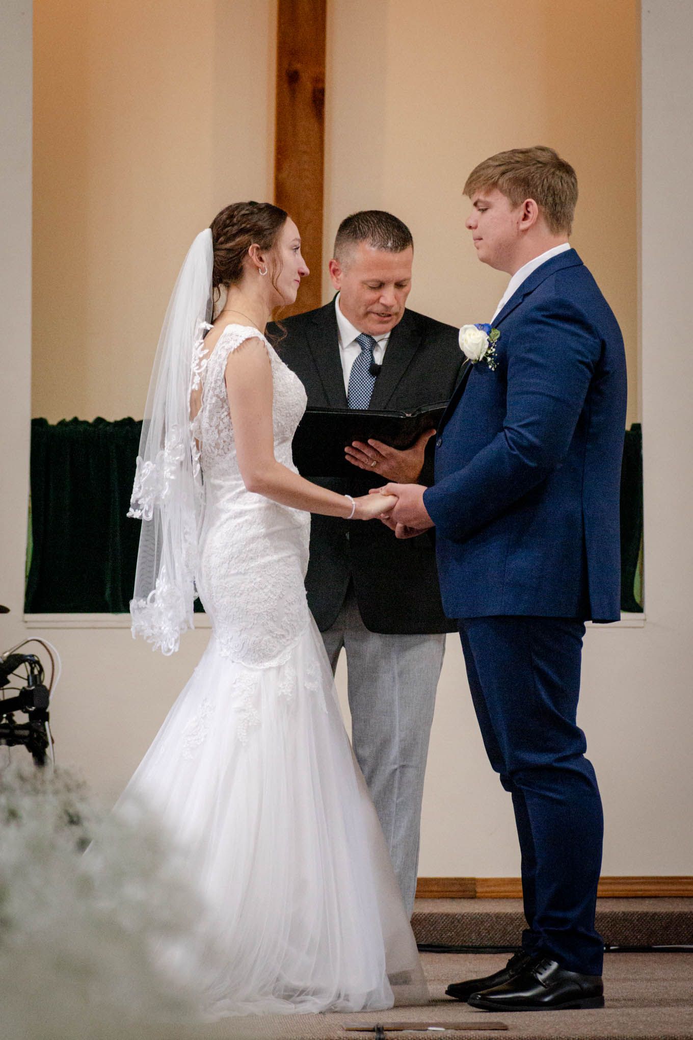 A bride and groom exchange vows at a church altar with an officiant during their wedding ceremony.