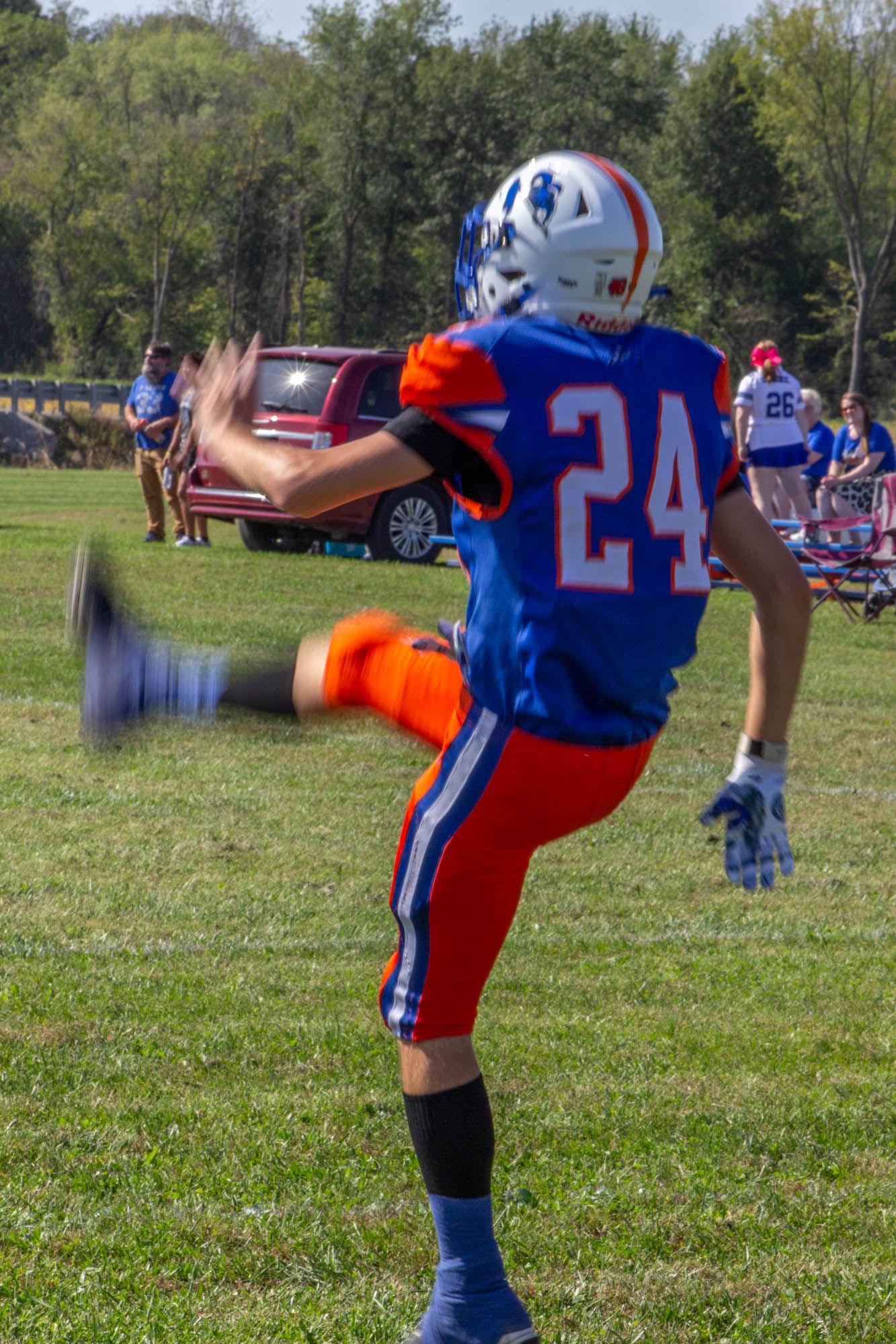 Football player #24 in blue and orange Pioneers uniform kicking during a youth football game outdoors.