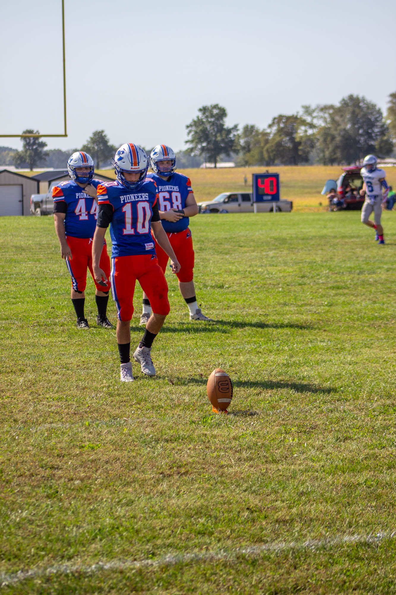 Pioneers football players #44, #10, and #68 line up near a football on the field during a game.