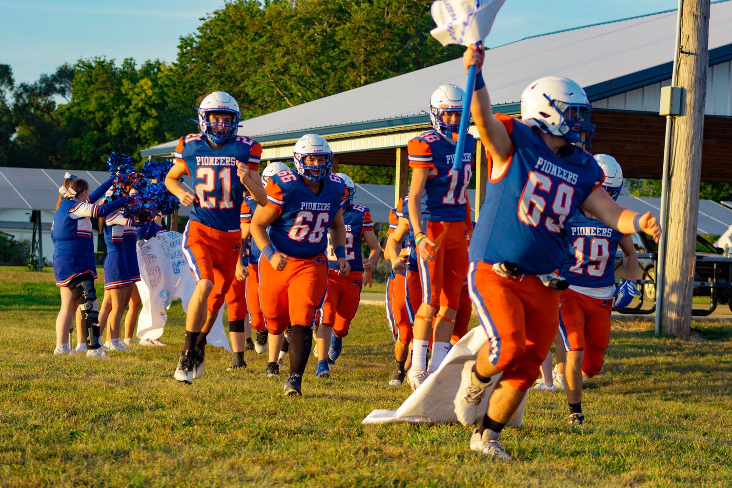 Pioneer football team in blue and orange uniforms runs onto the field at the start of a game.