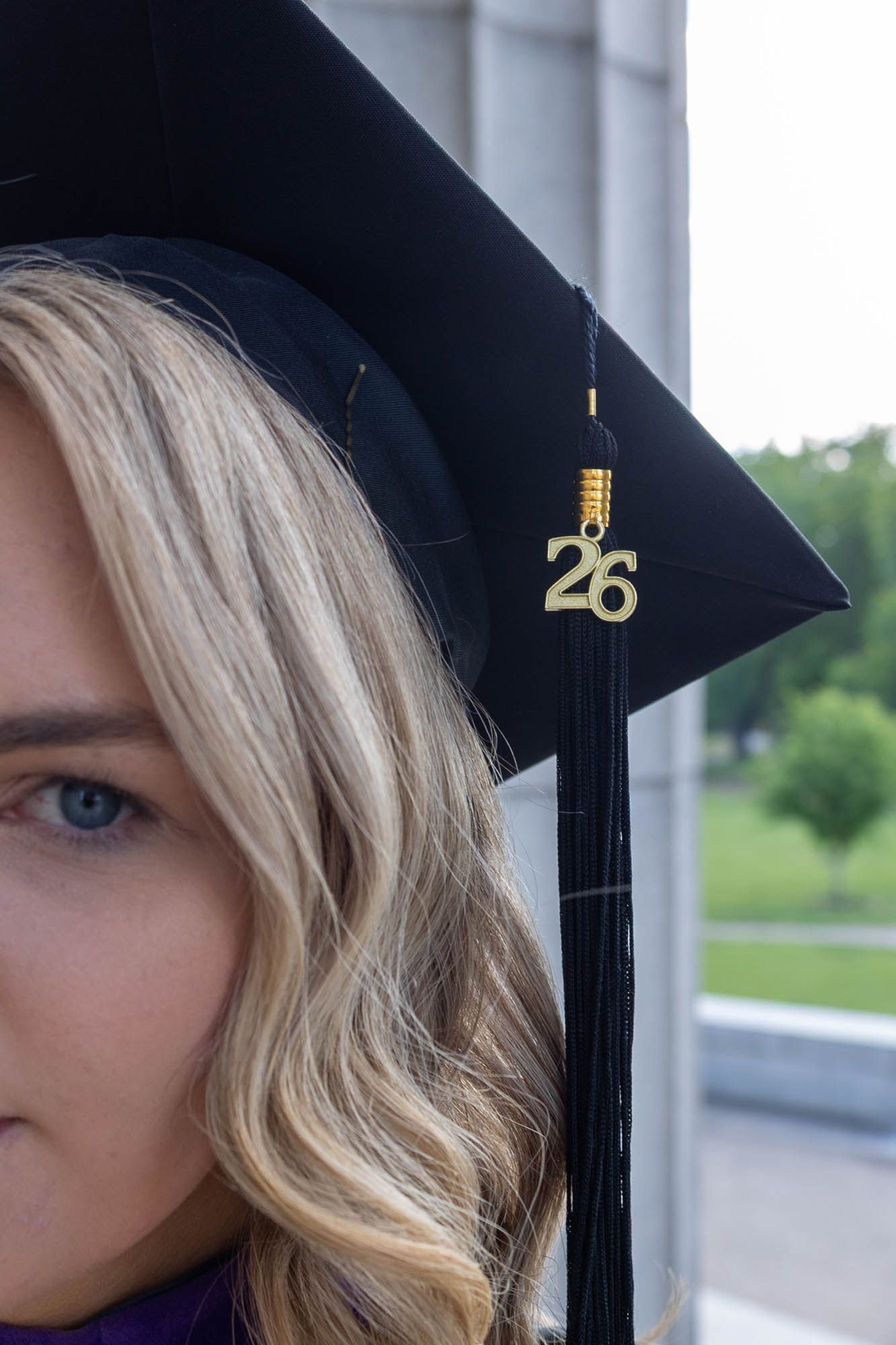 Close-up of a blonde woman wearing a black graduation cap with gold '26' tassel charm, class of 2026.