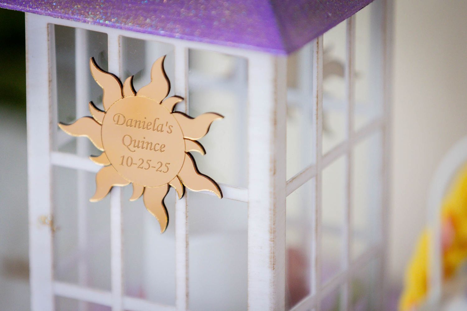 Wooden sun-shaped sign reading Daniela's Quince 10-25-25 on a white decorative birdcage with purple accents.