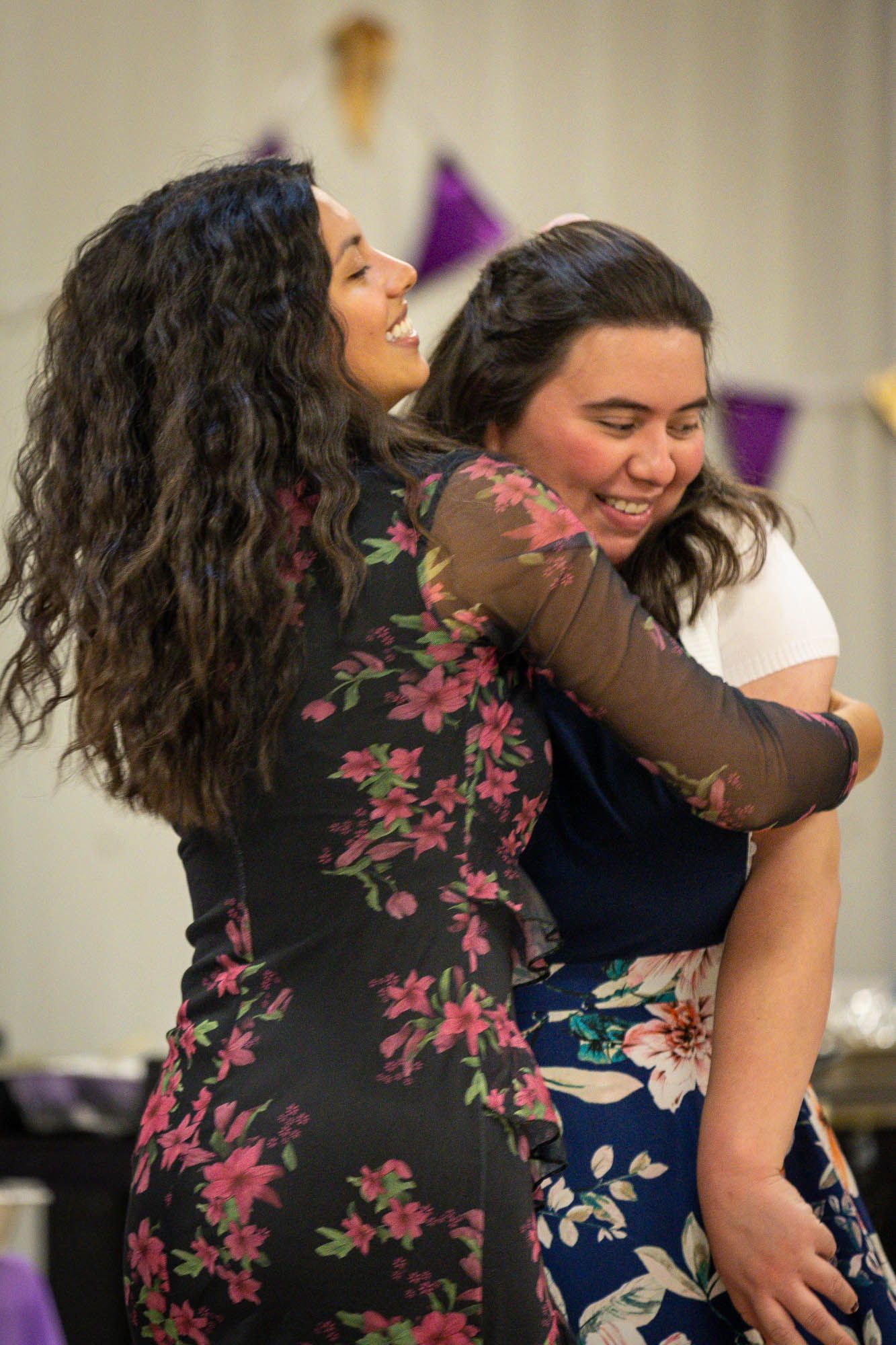 Two young women share a warm embrace and smile together at a quinceañera reception party.