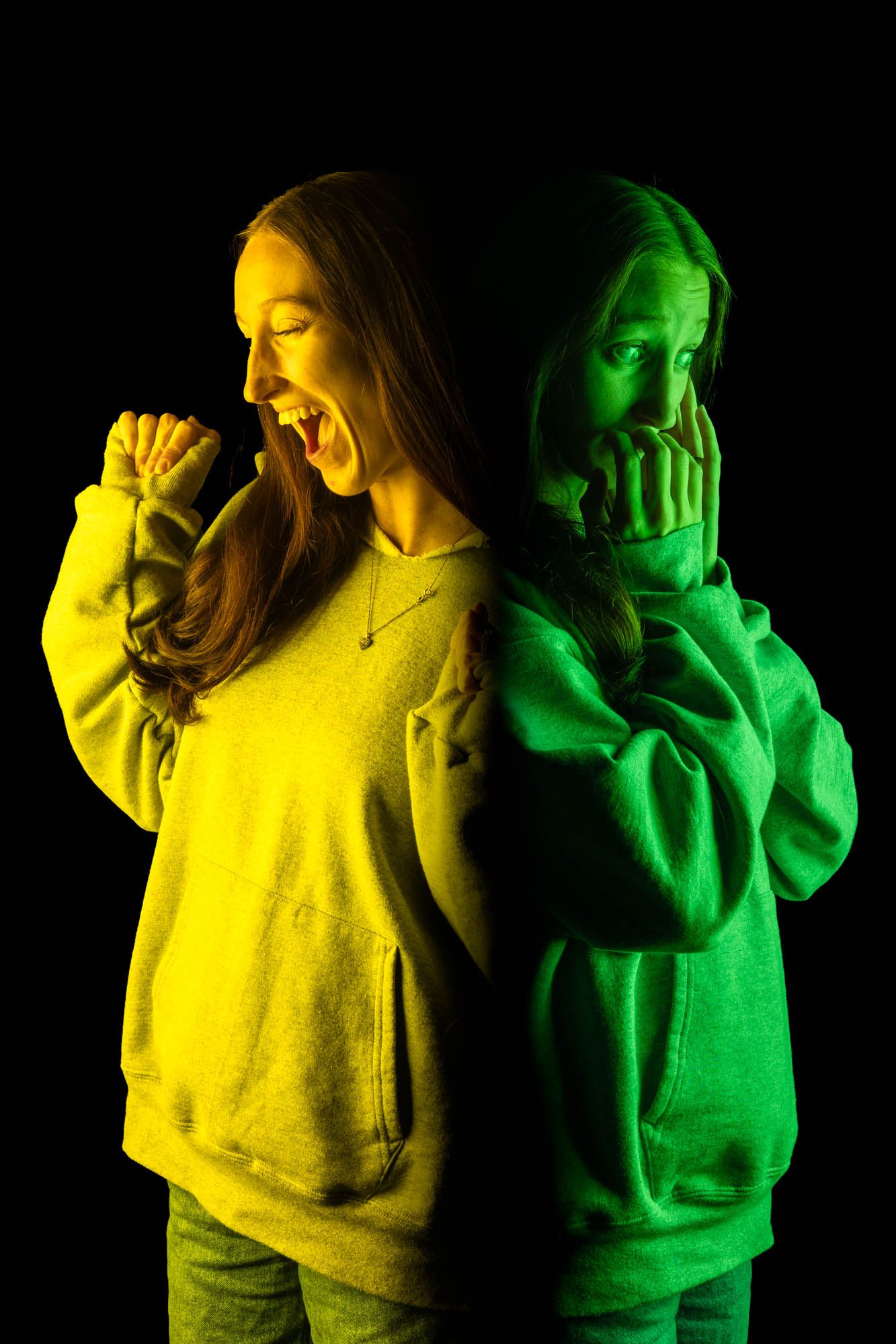 Young woman in hoodie photographed back-to-back in yellow and green light showing anger and fear emotions.