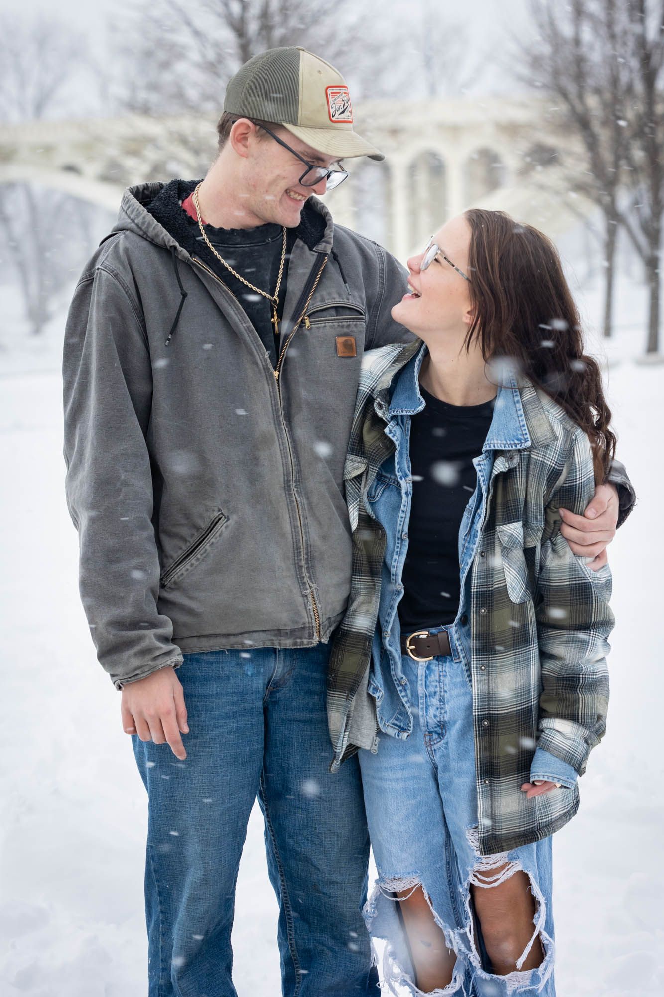 Young couple smiling at each other affectionately during a romantic winter snow session.