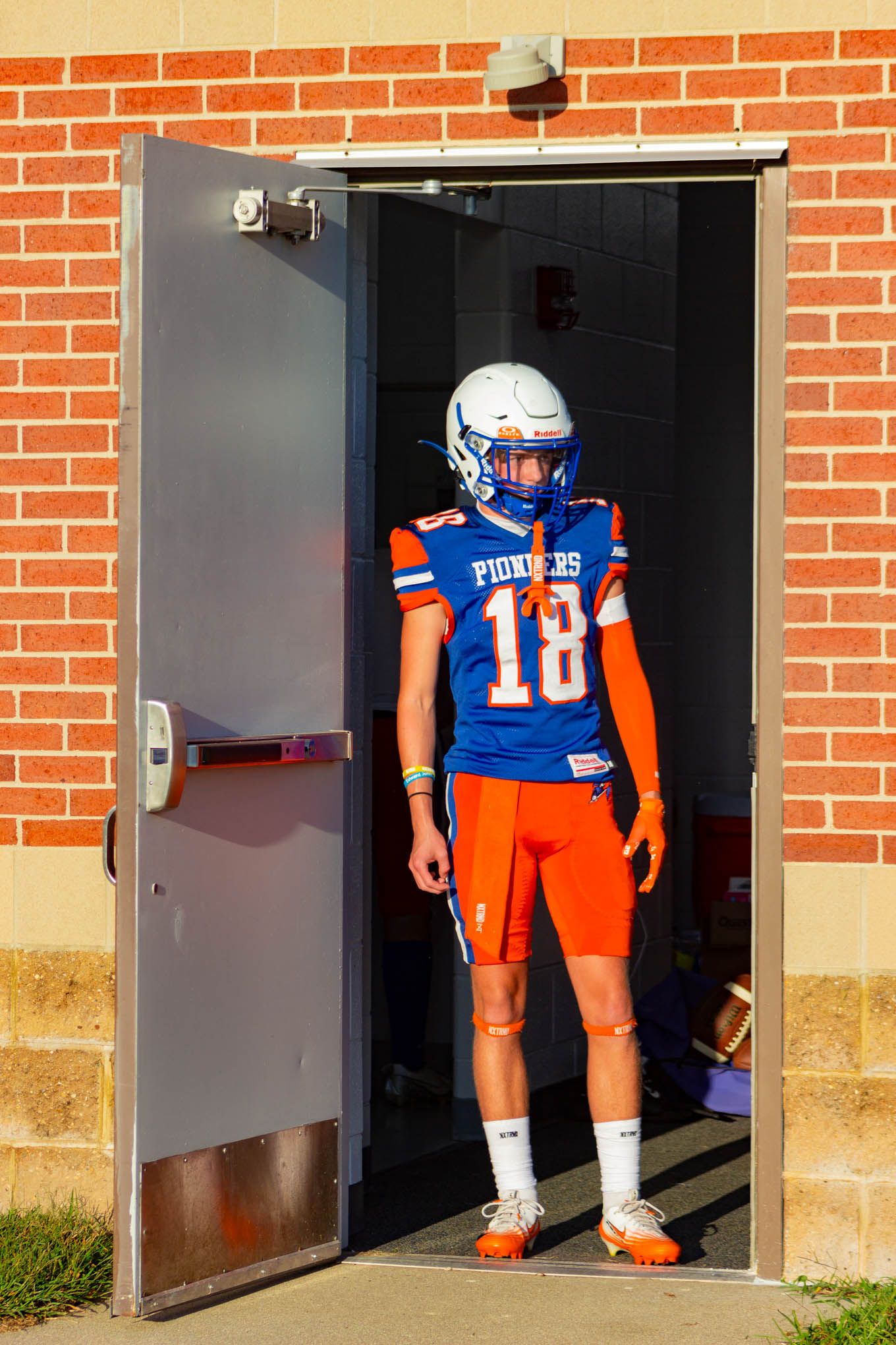 Pioneers football player number 18 in blue and orange uniform stands in a doorway.