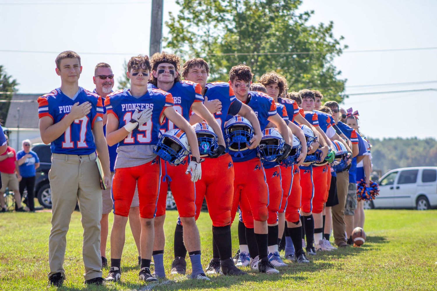 Pioneers youth football team lines up together on the field holding helmets before a game.