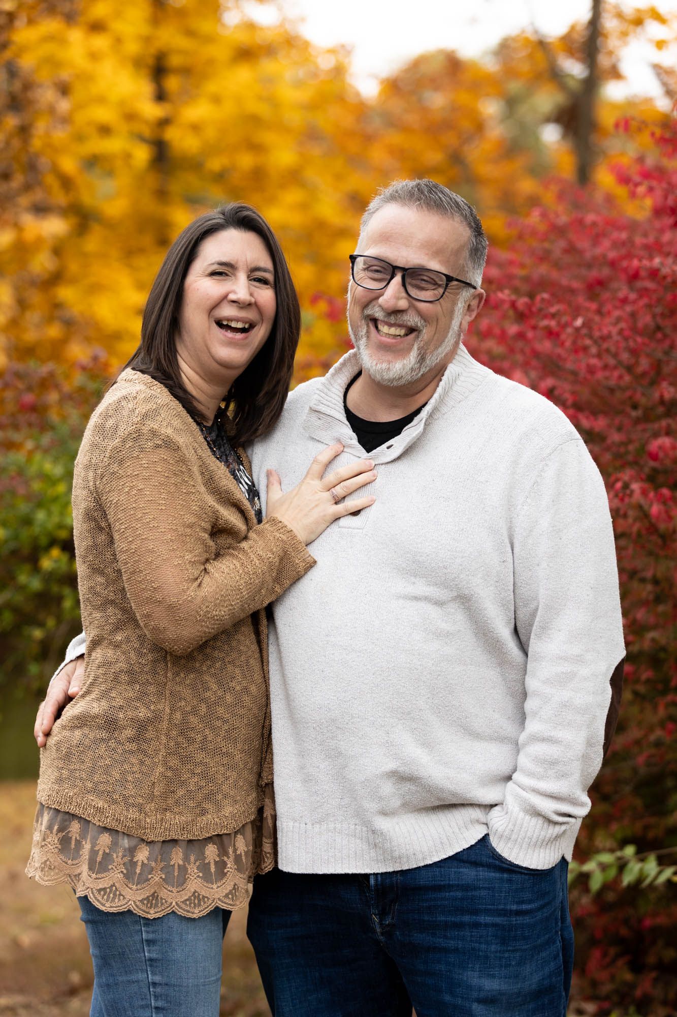 Happy middle-aged couple laughing together outdoors surrounded by vibrant autumn foliage.