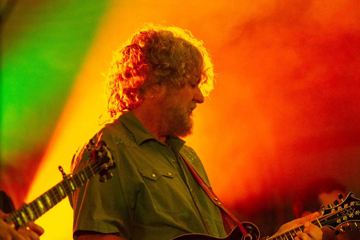 Bearded guitarist performs on stage bathed in dramatic red and green stage lighting.