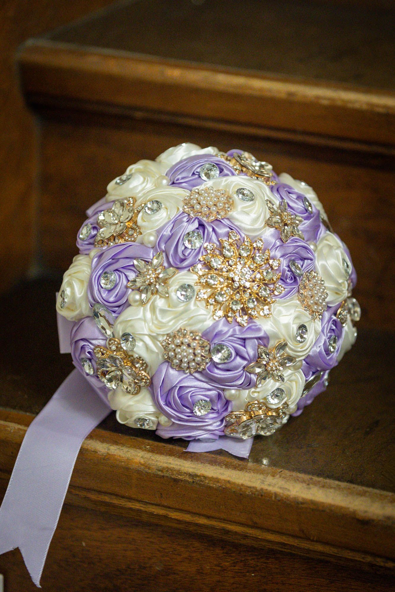 Elegant lavender and ivory satin rose brooch bouquet with gold and crystal jeweled accents for a wedding.