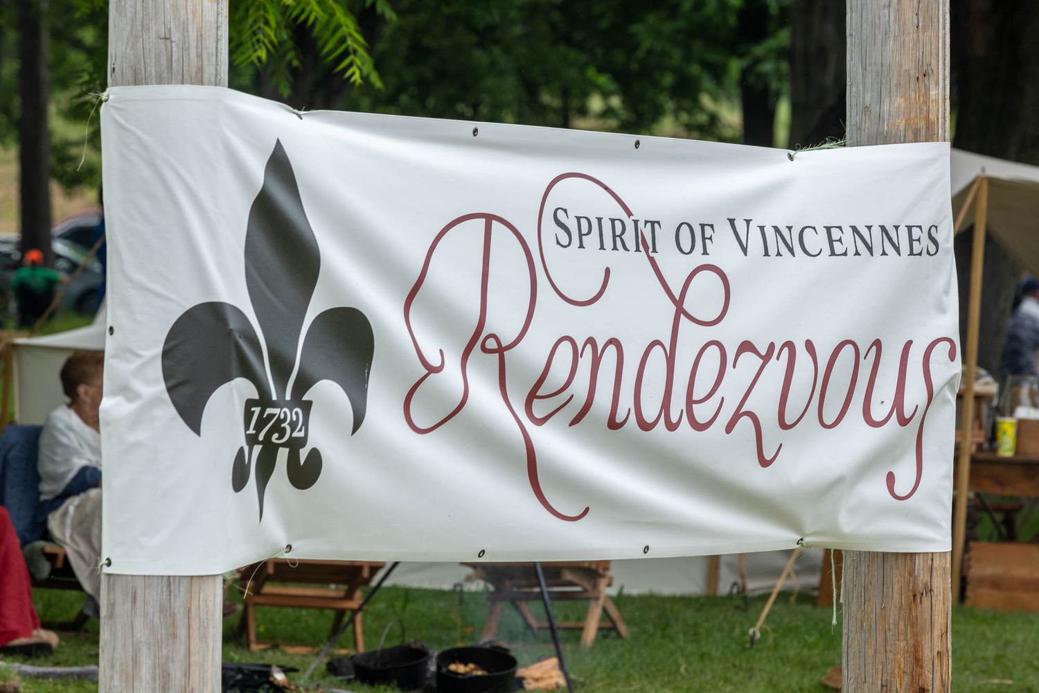 Spirit of Vincennes Rendezvous 1732 banner with fleur-de-lis logo displayed outdoors at a historical reenactment event.