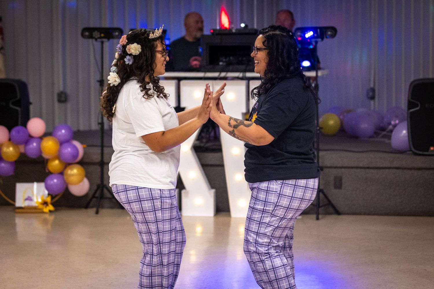 Two women in matching plaid pants share a dance together on the dance floor at a quinceañera celebration.