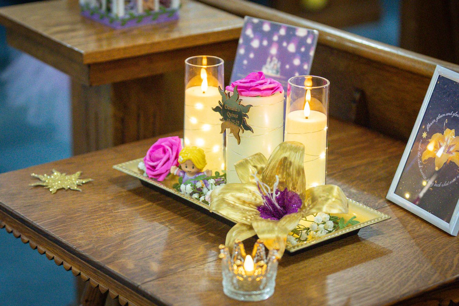 Elegant quinceañera centerpiece with lit candles, pink roses, and gold floral decorations on a wooden table.