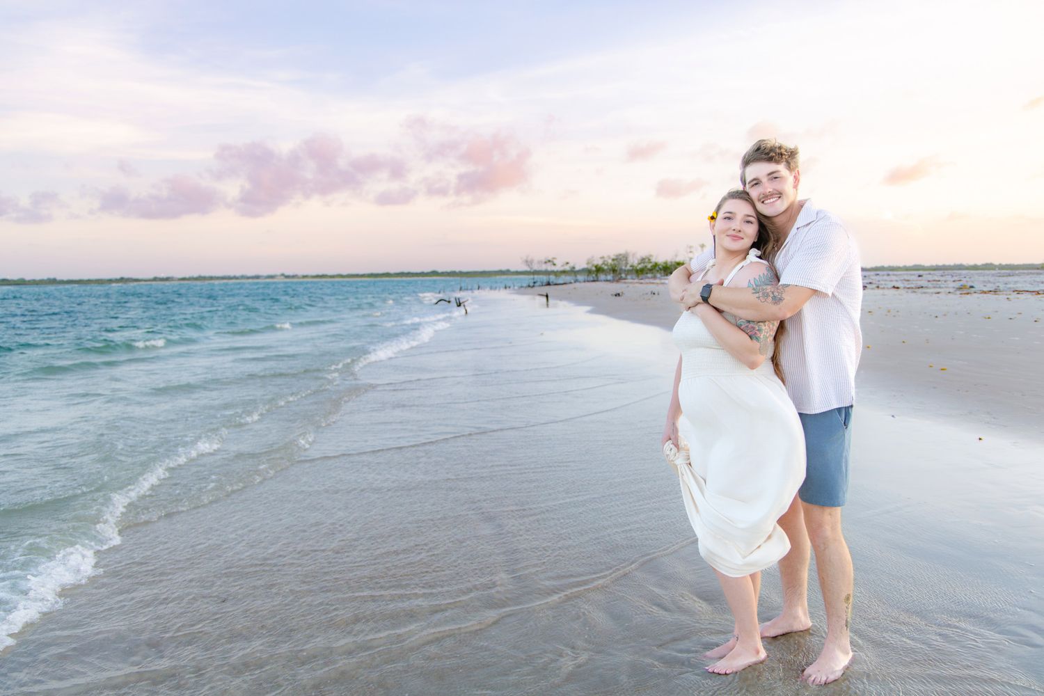 Couple embracing on a beach at sunset with turquoise water.