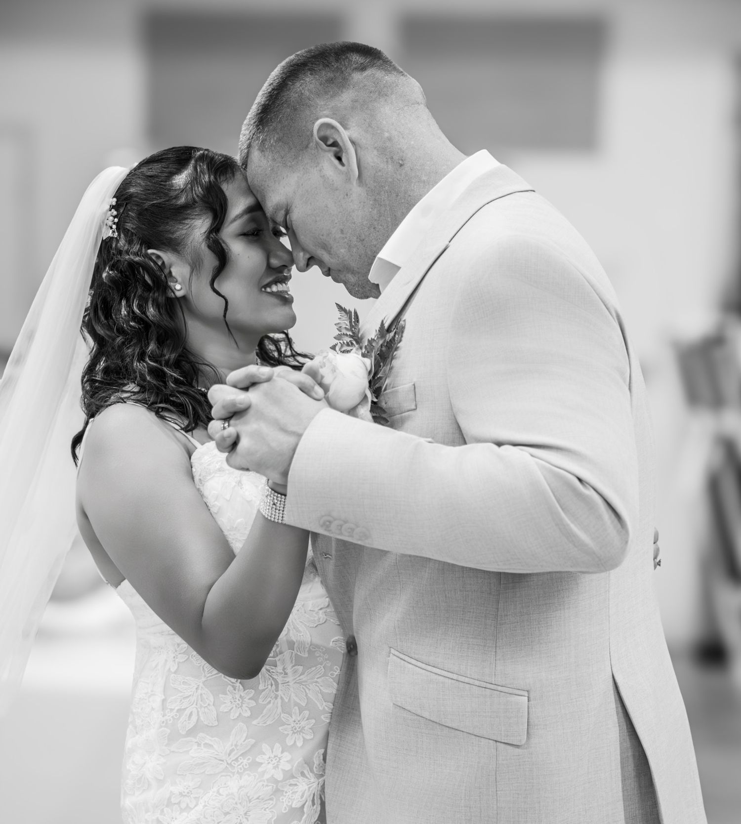 Black and white photo of bride and groom sharing first dance, foreheads touching, holding hands at wedding reception.