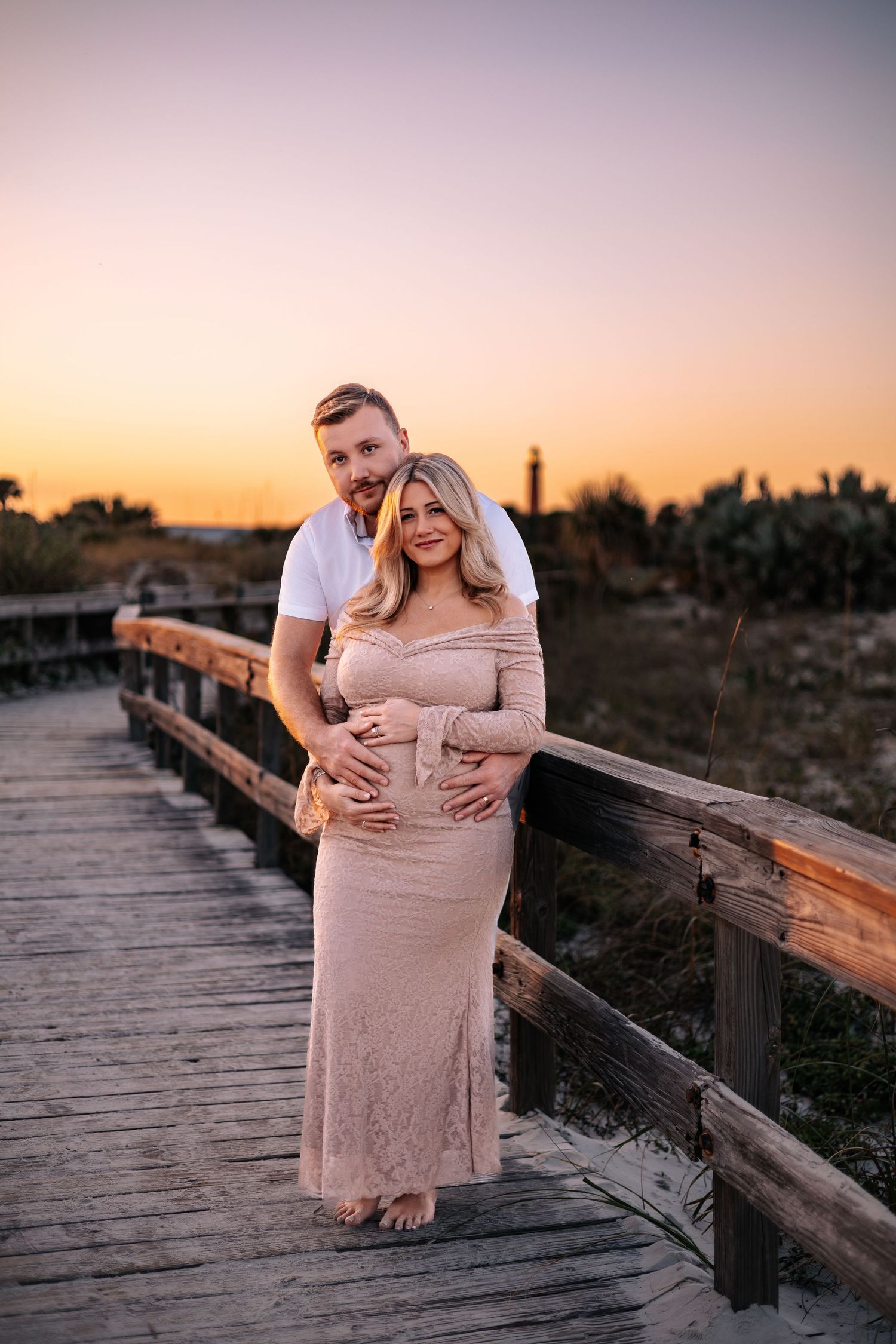 A couple embraces on a wooden boardwalk at sunset, creating a romantic silhouette against the warm sky.