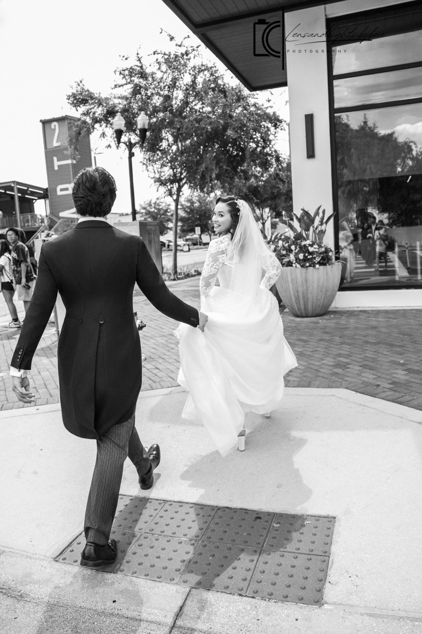 Black and white photo of a bride in white gown and veil walking hand in hand with groom in suit outdoors.