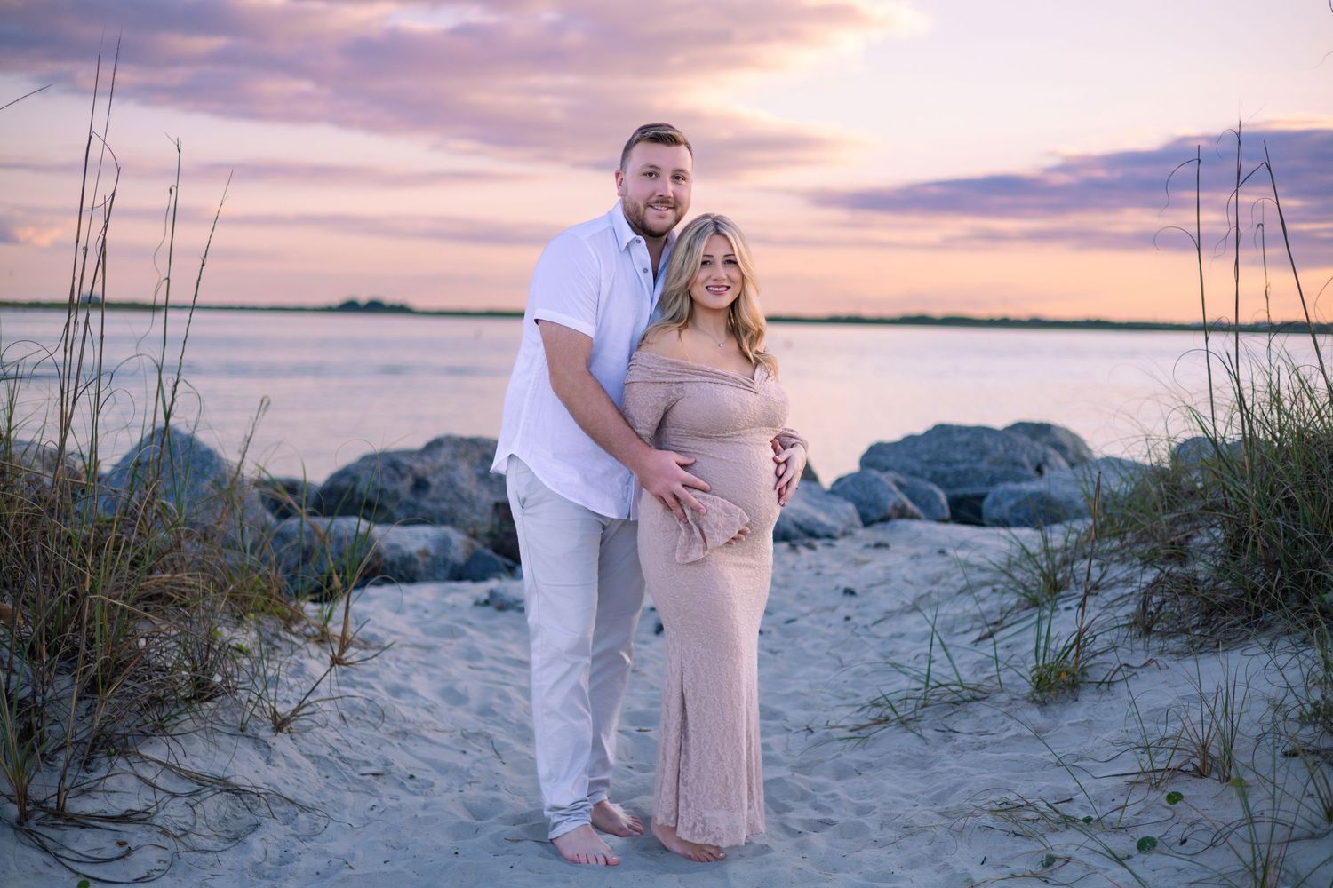 Couple walking on sandy beach path through sea oats during a dreamy pink sunset.