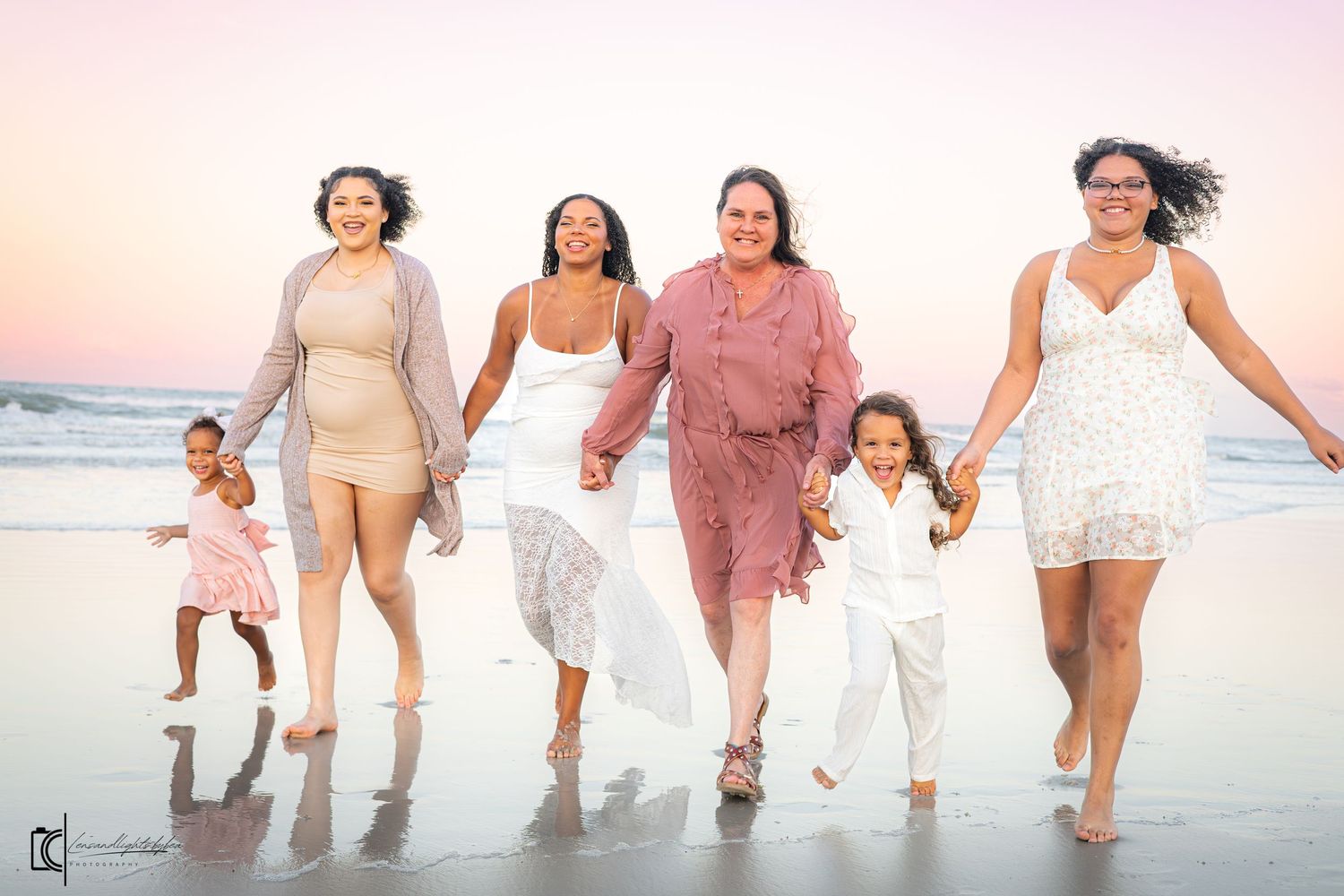 A happy family wearing white and beige outfits walks together along the beach at sunset.