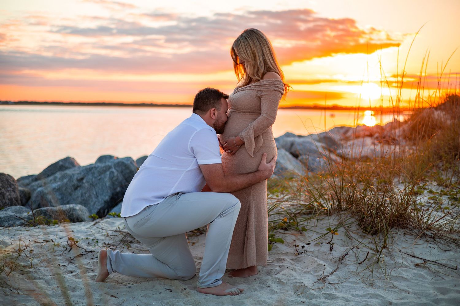 A romantic proposal moment unfolds on a sandy beach during a vibrant orange sunset.