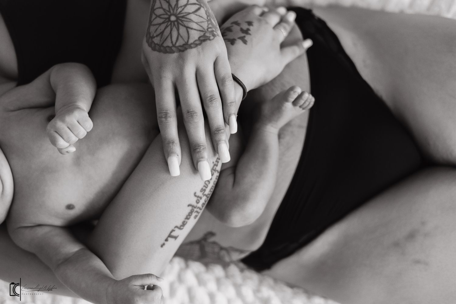 Black and white close-up of a parent's tattooed hand gently touching a baby's bare torso.