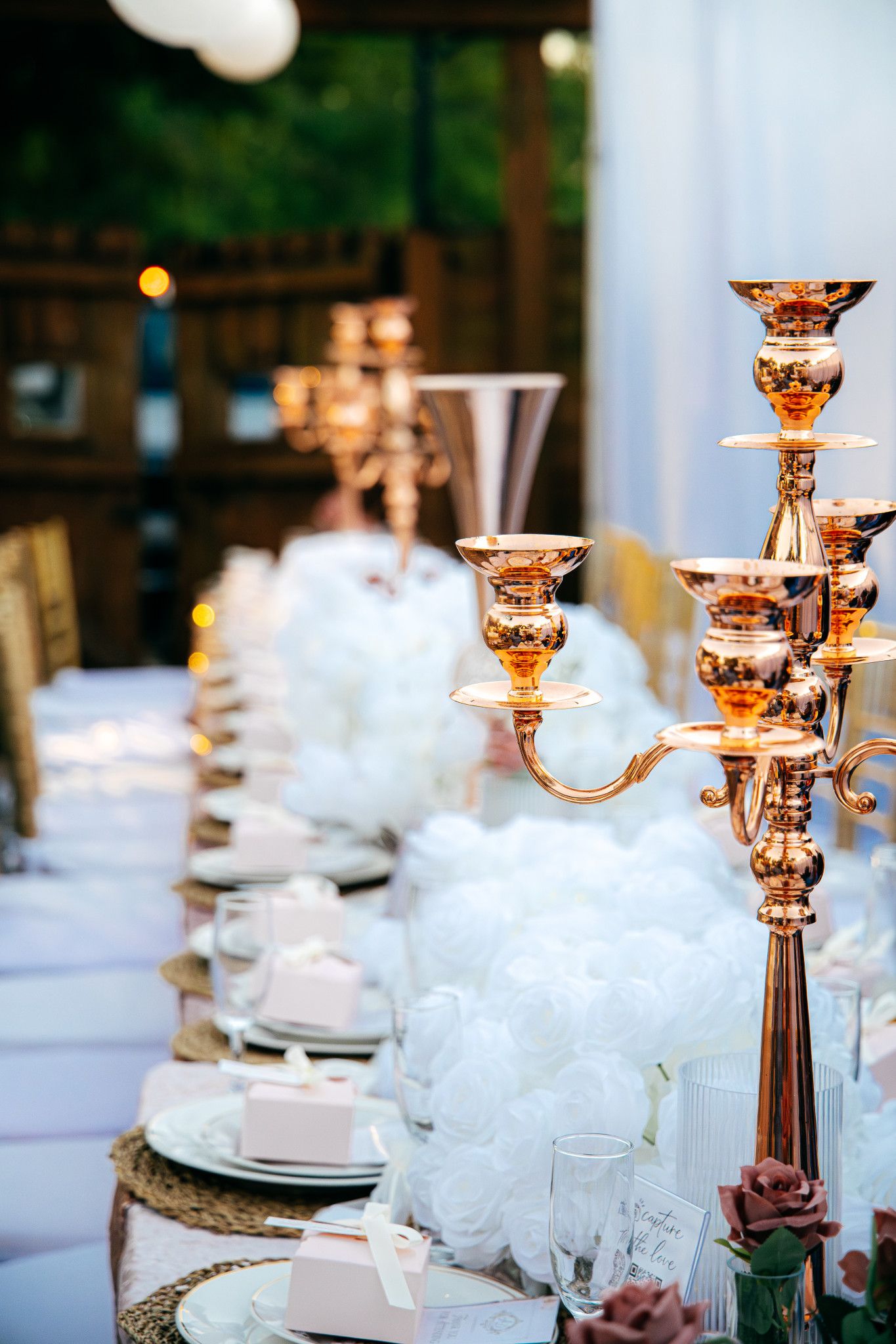 Elegant rose gold candelabras and white place settings adorn a formal dining table at an upscale wedding reception.