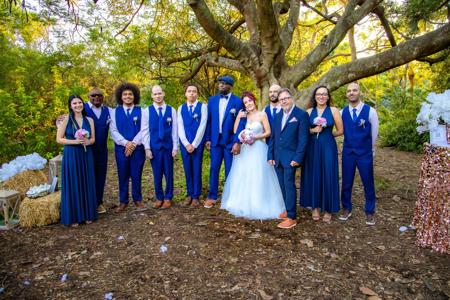 Wedding party in royal blue attire poses together under autumn trees during outdoor photo session.