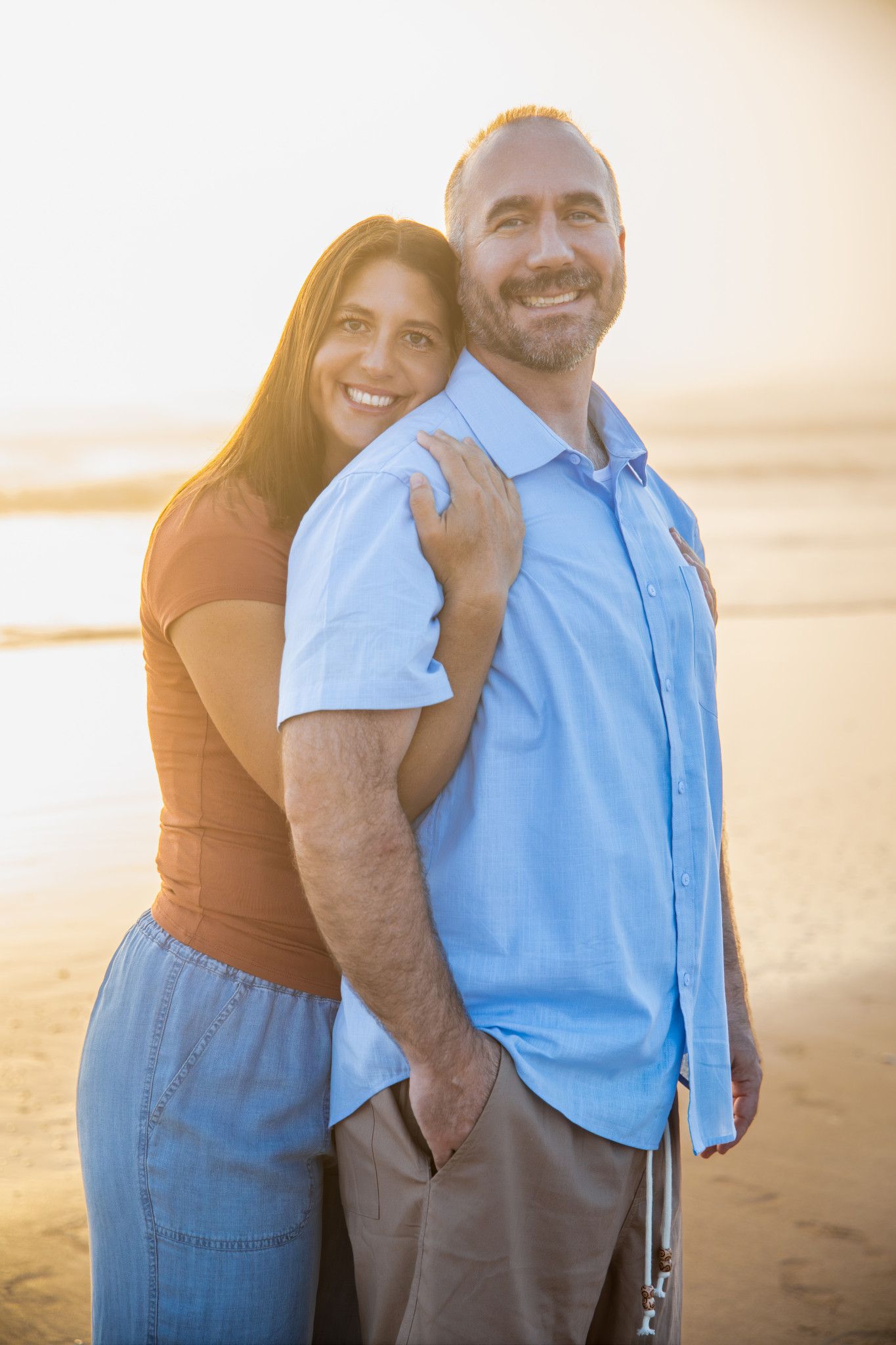 A couple embraces lovingly on a sandy beach during golden hour sunset.