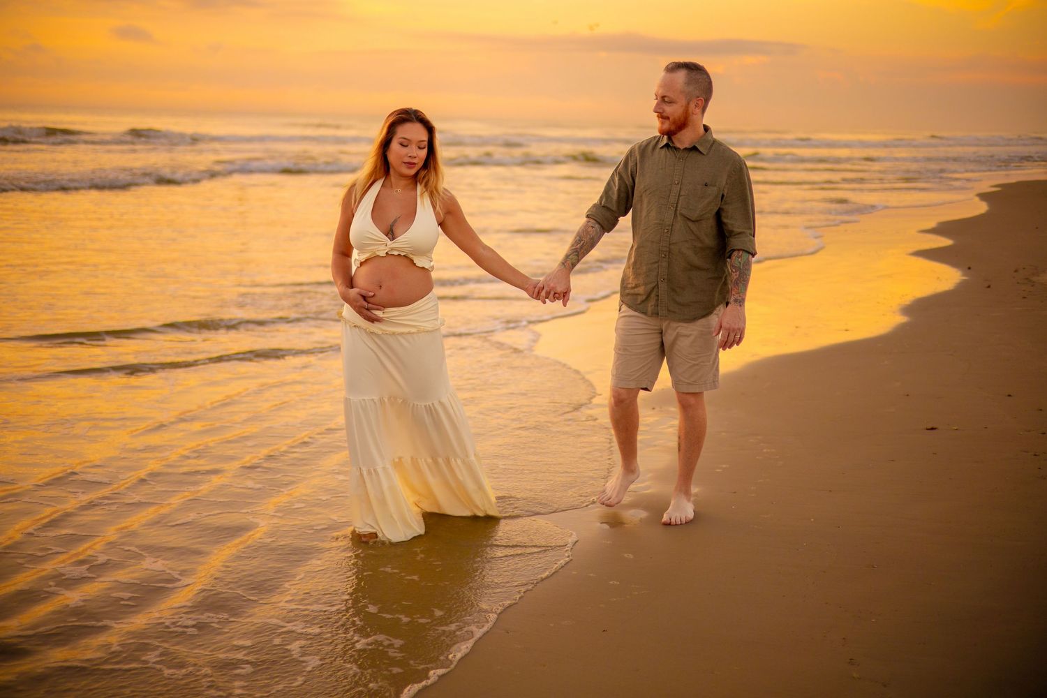 Romantic beach photoshoot at golden hour with couple walking along shoreline at sunset.